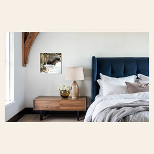 A piece of Big Sur art showing a waterfall photo hangs over a bedside table.