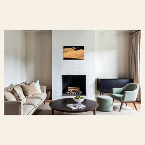 A piece of Colorado art showing a photo of Great Sand Dunes National Park hangs above a fireplace.