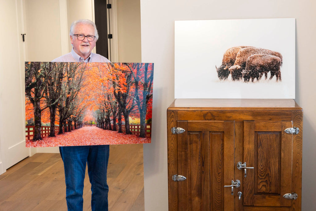 A collector with West Seattle artist Gesing's fine art photograph of fall colors at Rockwood Farm and a bison artwork.