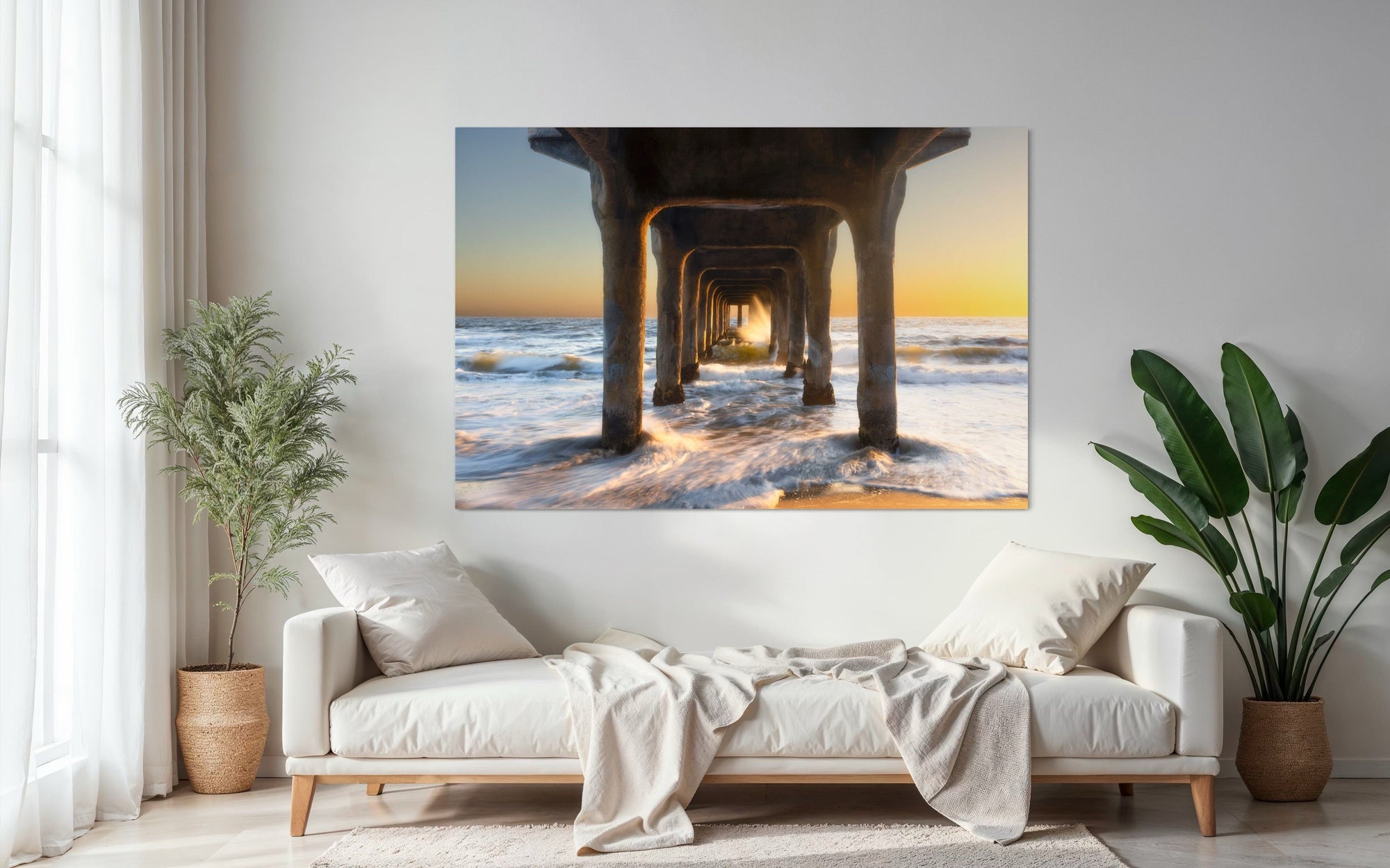 A piece of Southern California wall art showing a photo of a sunset at Manhattan Beach Pier hangs above a couch.