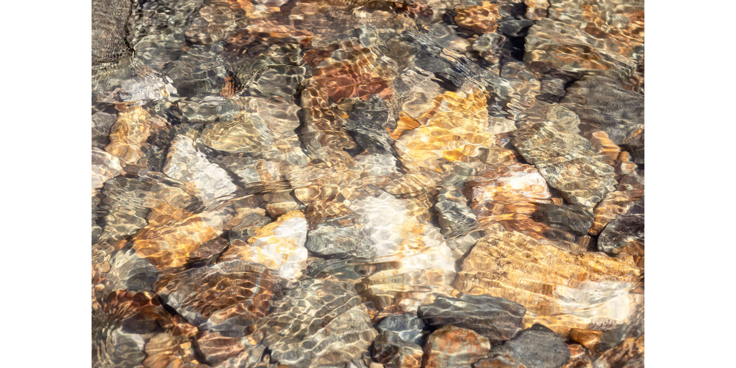 This piece of Telluride art shows glistening rocks in a Colorado River.